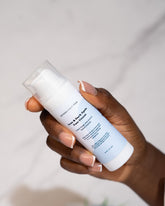 Acne & Dark Spots Face Cream in hand against a marble background.